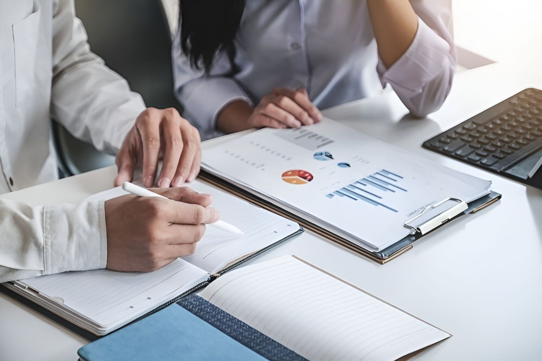 A Man And A Woman Are Sitting At A Table Looking At A Clipboard — Grant Finance Solutions In Highlands, QLD