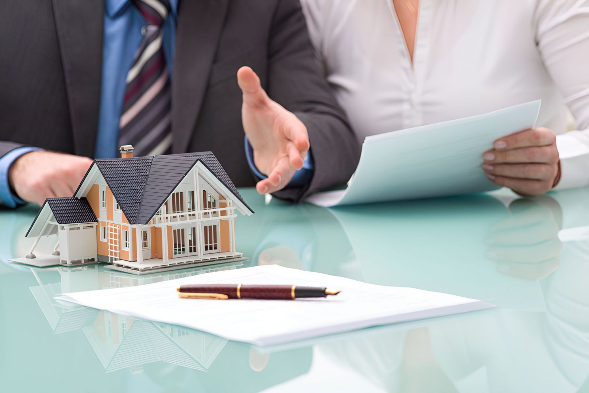 A Man And A Woman Are Sitting At A Table With A Model House On It — Grant Finance Solutions In Toowoomba, QLD