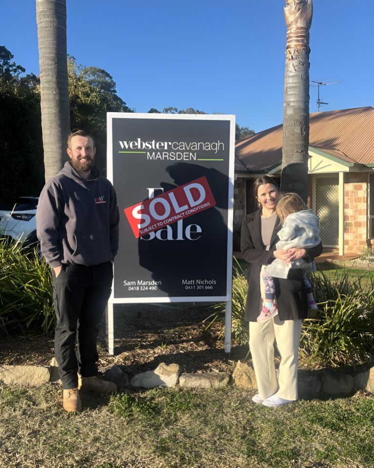 A Man And A Woman Are Standing In Front Of A Sold Sign — Grant Finance Solutions In Toowoomba, QLD