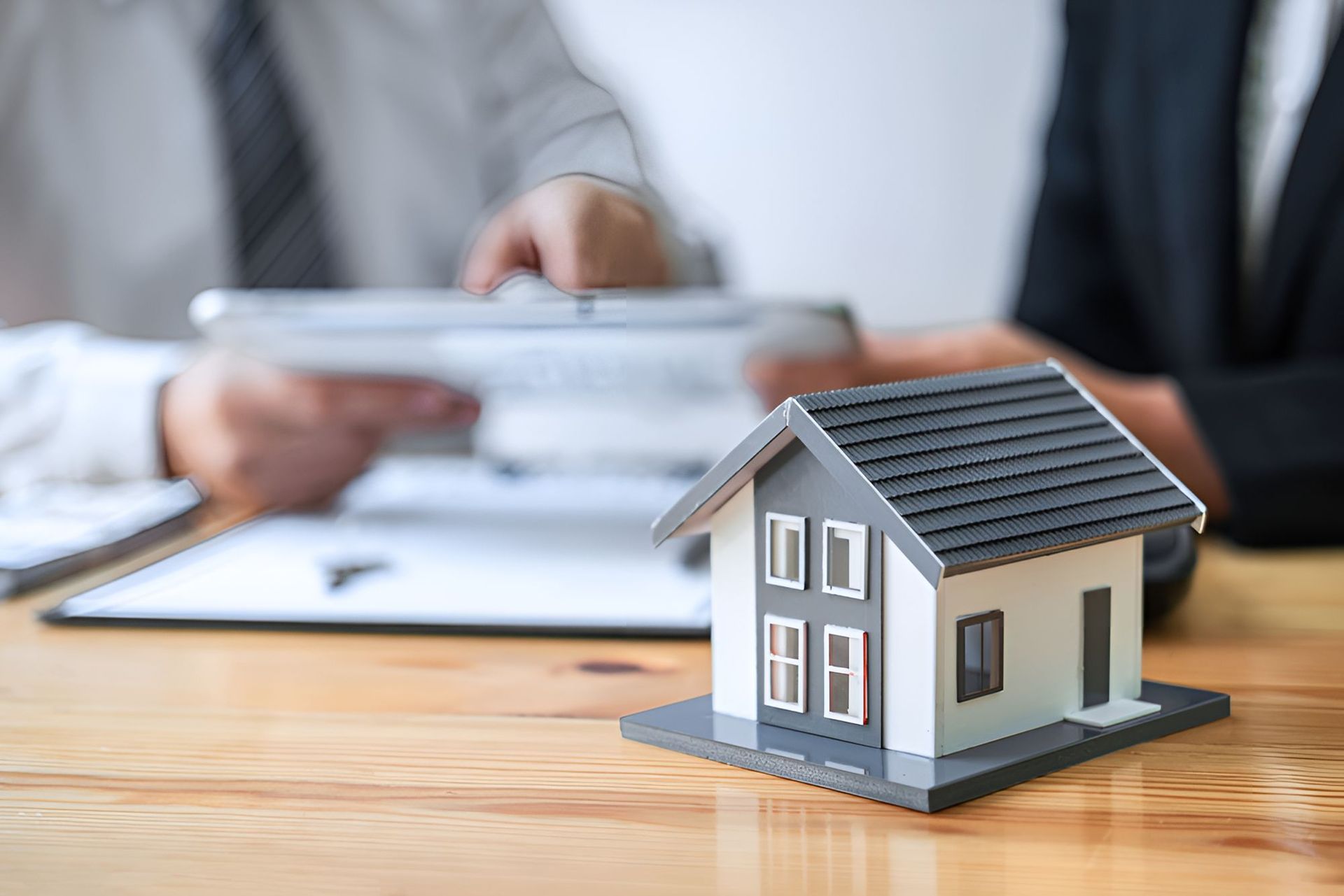 A Couple Of People Are Sitting At A Table With A Model House On It — Grant Finance Solutions In Toowoomba, QLD