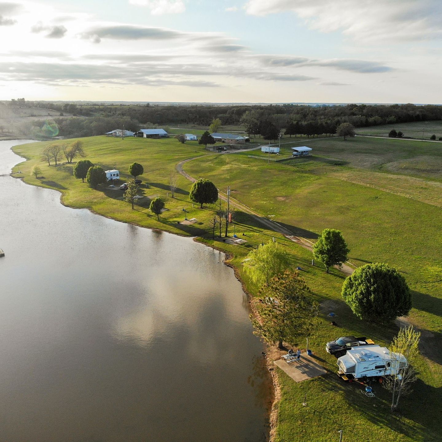 A scenic view of a lake and green field with buildings under a cloudy sky.