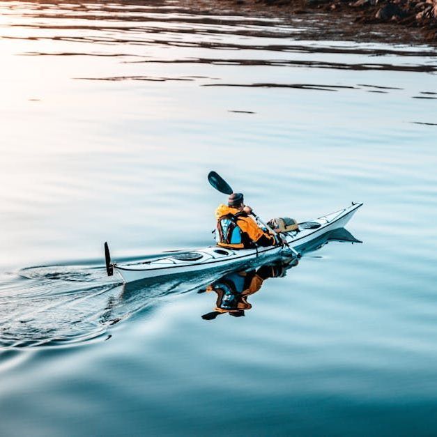 Person kayaking on calm water, reflected in the surface.