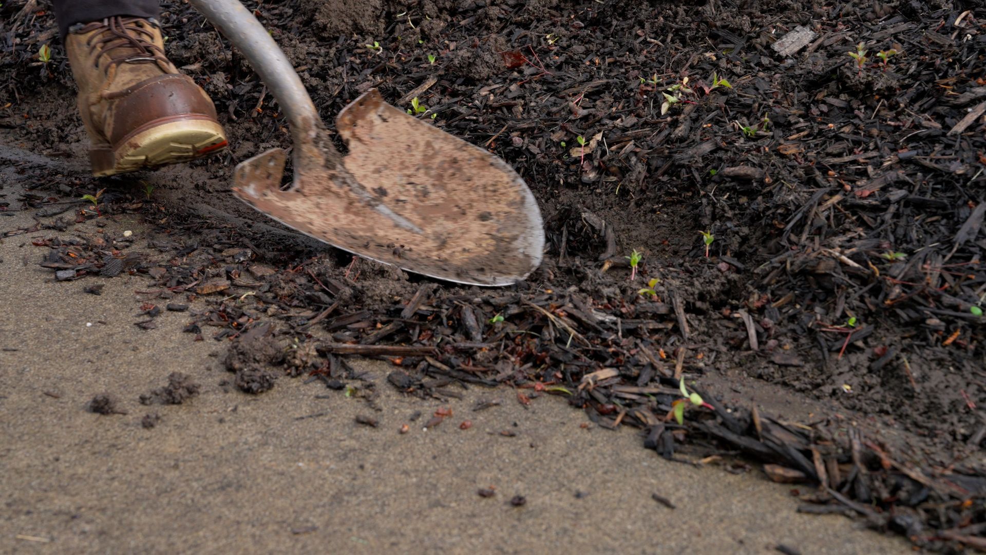 A shovel with a muddy blade rests beside wet soil and a concrete edge