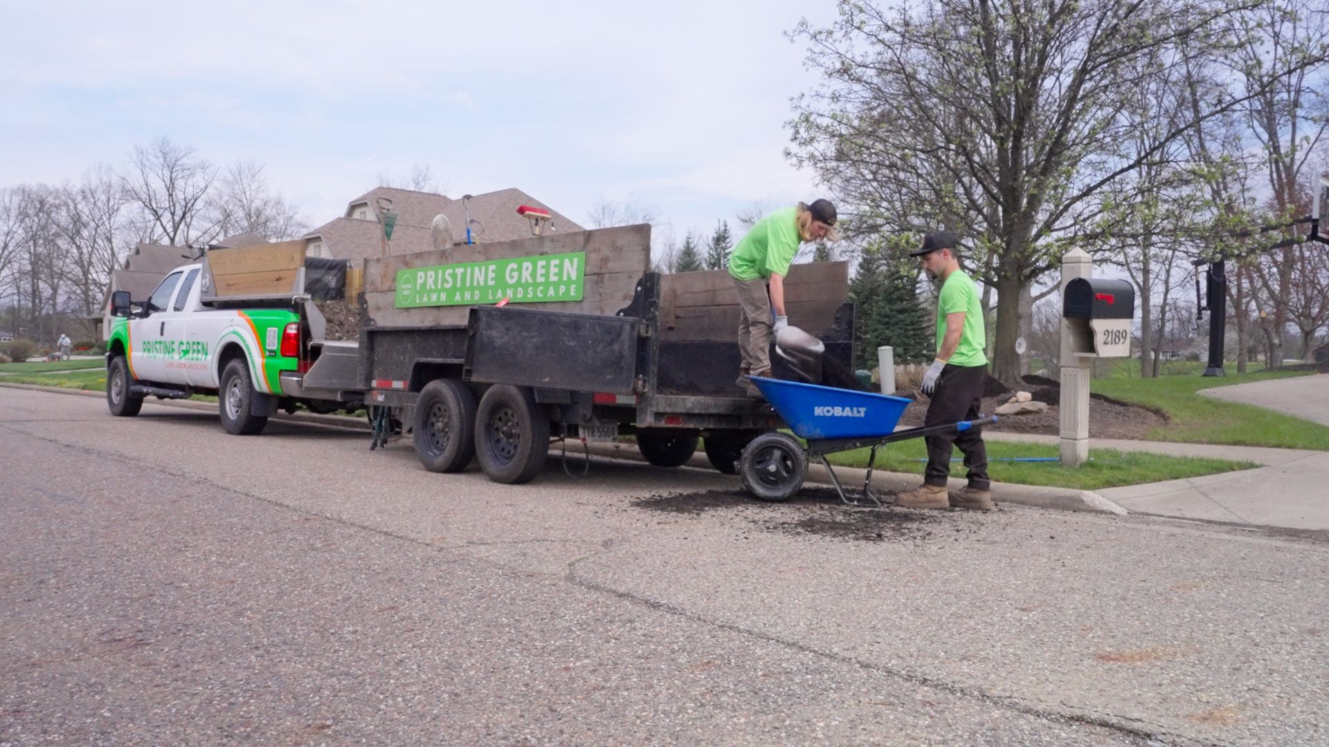 City work crew loads brush into a truck and trailer on a suburban street.