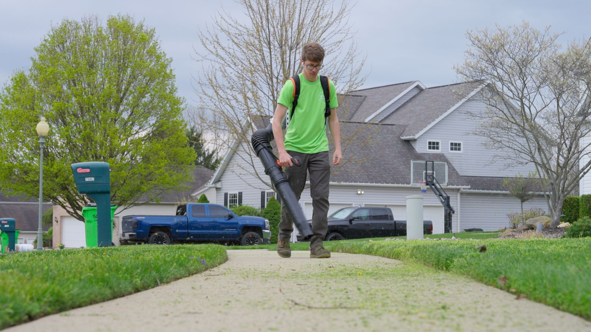 Person walking on a sidewalk in a suburban neighborhood, wearing a bright green backpack.