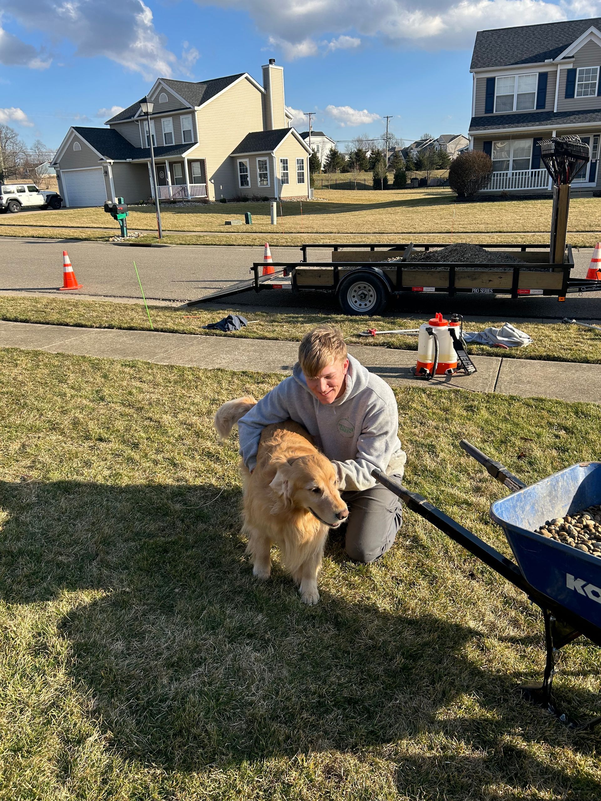A man is kneeling down next to a dog in a grassy field.