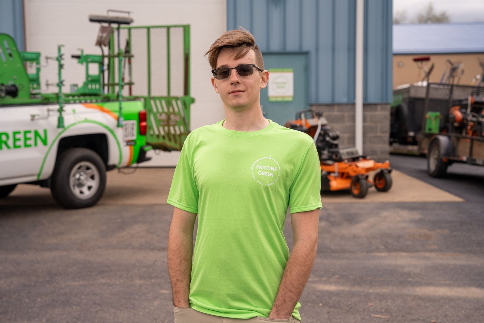Man in neon green shirt and sunglasses standing in an industrial yard with trucks and equipment in the background