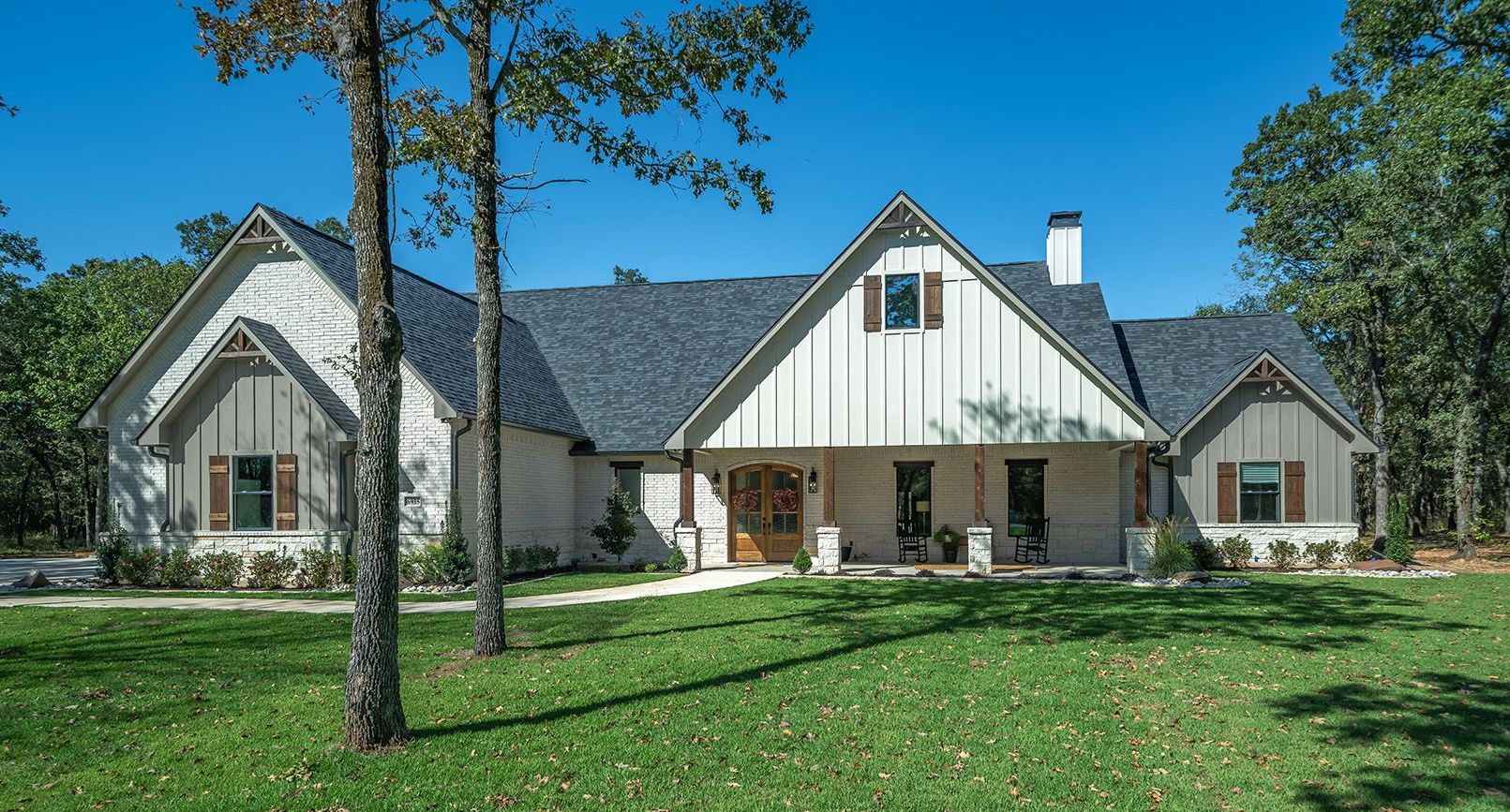 A large white house with a gray roof is sitting in the middle of a lush green field.