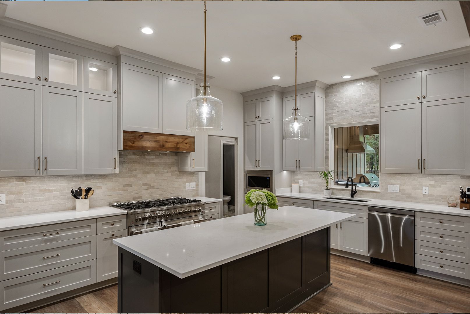 A kitchen with gray cabinets , white counter tops , stainless steel appliances and a large island.