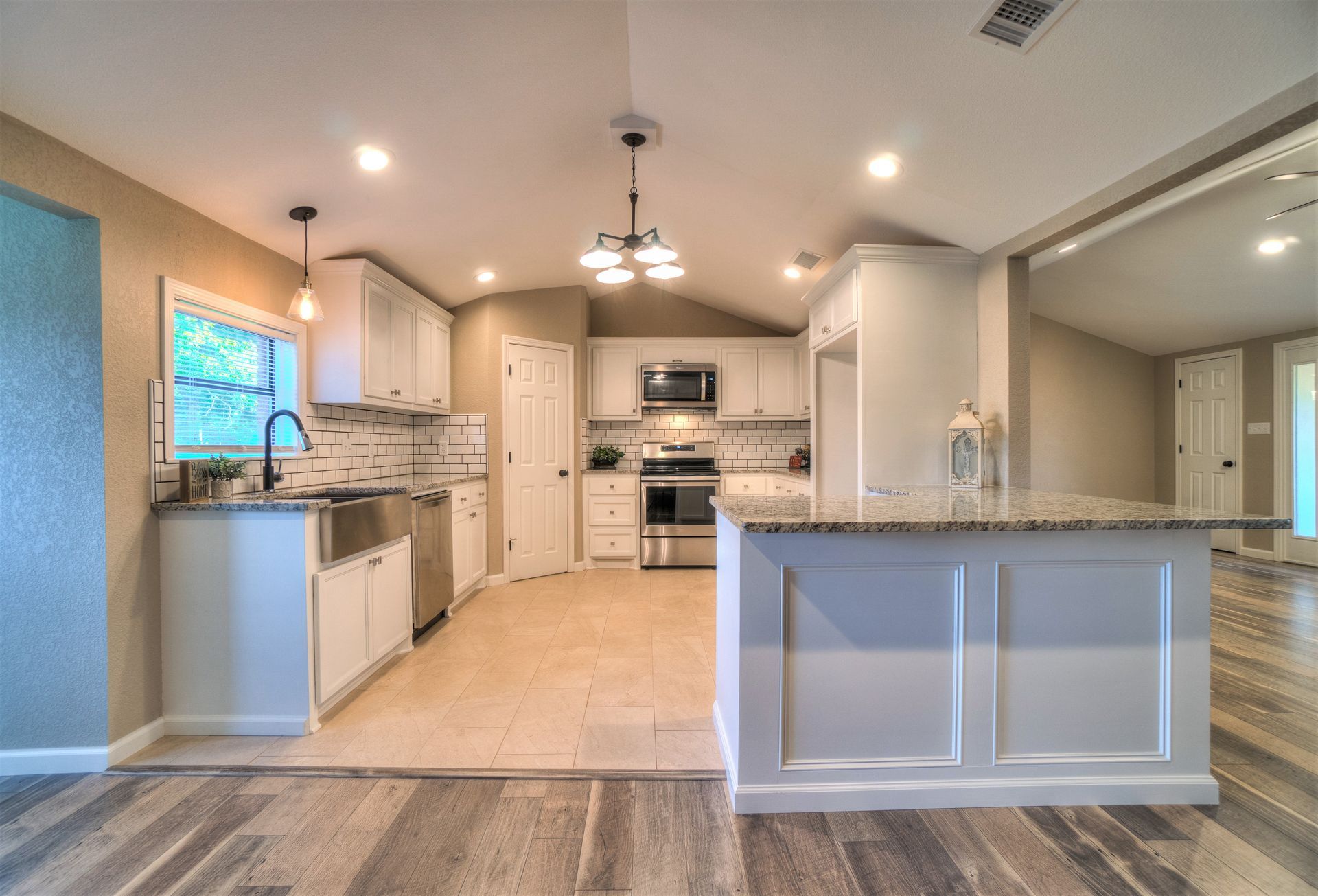 A kitchen with white cabinets , granite counter tops , stainless steel appliances and a large island.