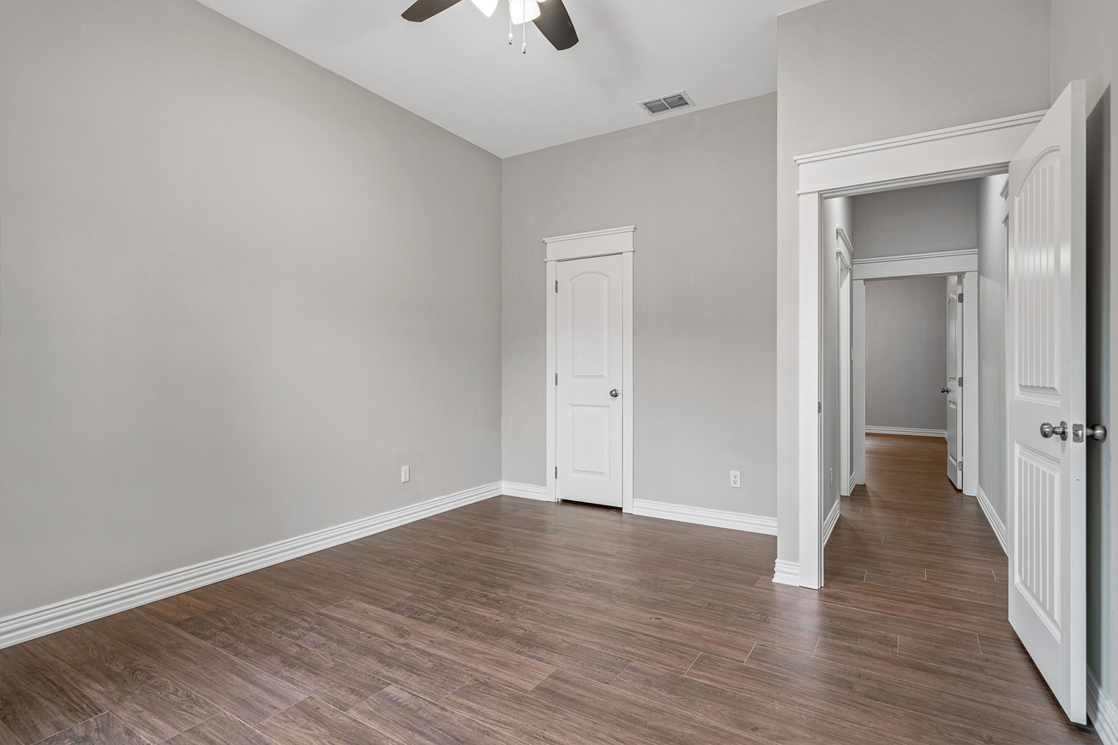 An empty bedroom with hardwood floors and a ceiling fan.