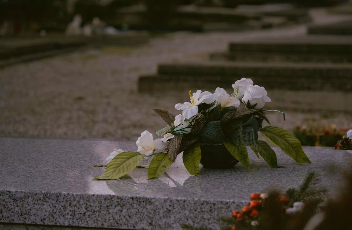 White floral tribute resting on a gravestone in a cemetery, representing funeral and cremation services and memorial remembrance