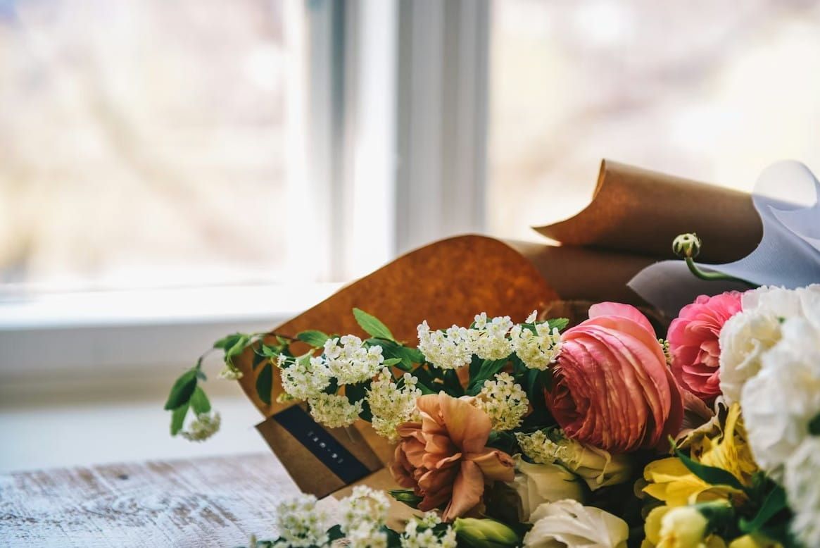 Soft floral arrangement for funeral and cremation services near a window, featuring elegant pink, white, and yellow sympathy flowers