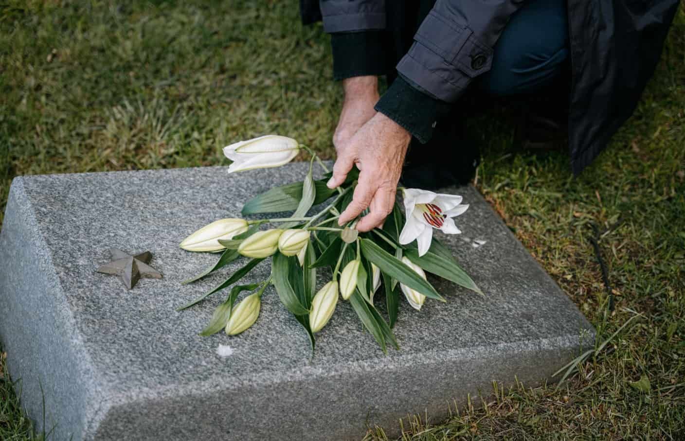 Person placing white lilies on a gravestone during a memorial, representing Carmel IN funeral and cremation services