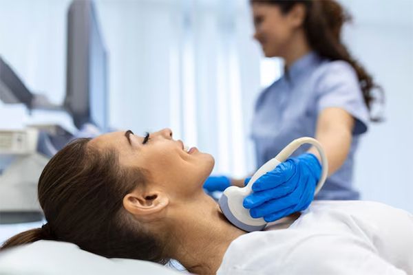 Patient undergoing neck ultrasound examination in a clinic, with a technician using a probe.