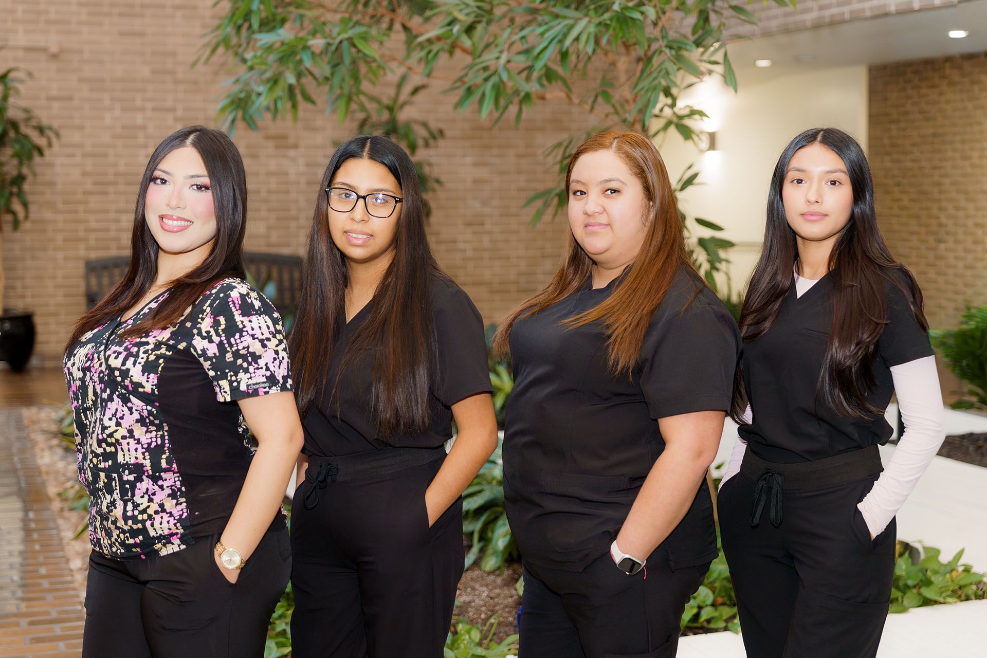 Four professionals standing indoors, dressed in black, posing in front of greenery.