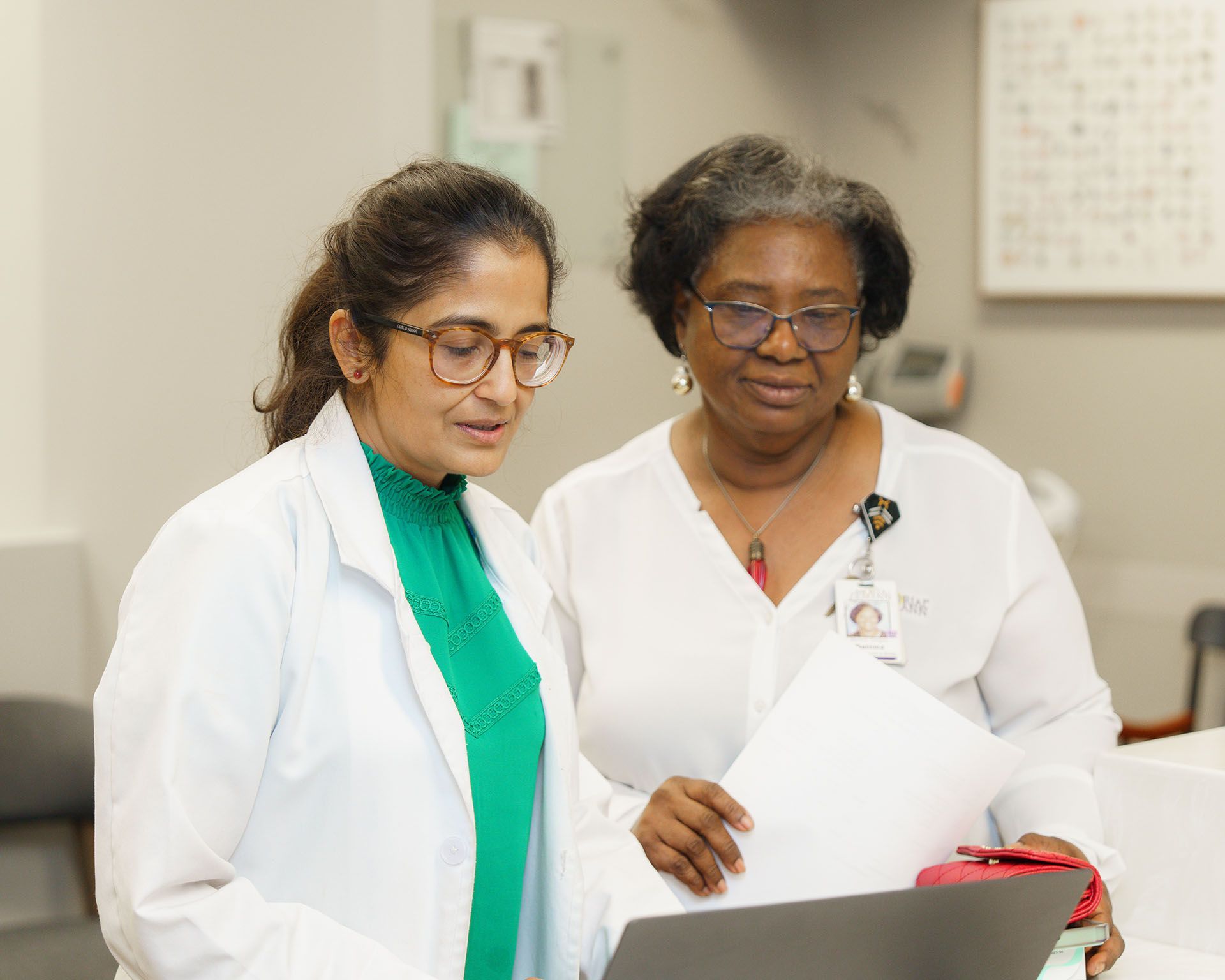 Two women in white coats reviewing documents together in a clinical setting