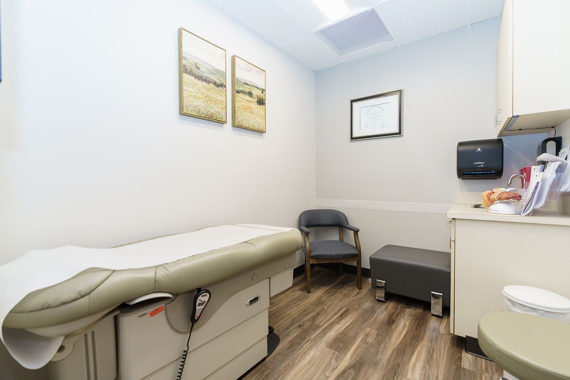 Medical exam room with exam table, chair, cabinets, and wall art