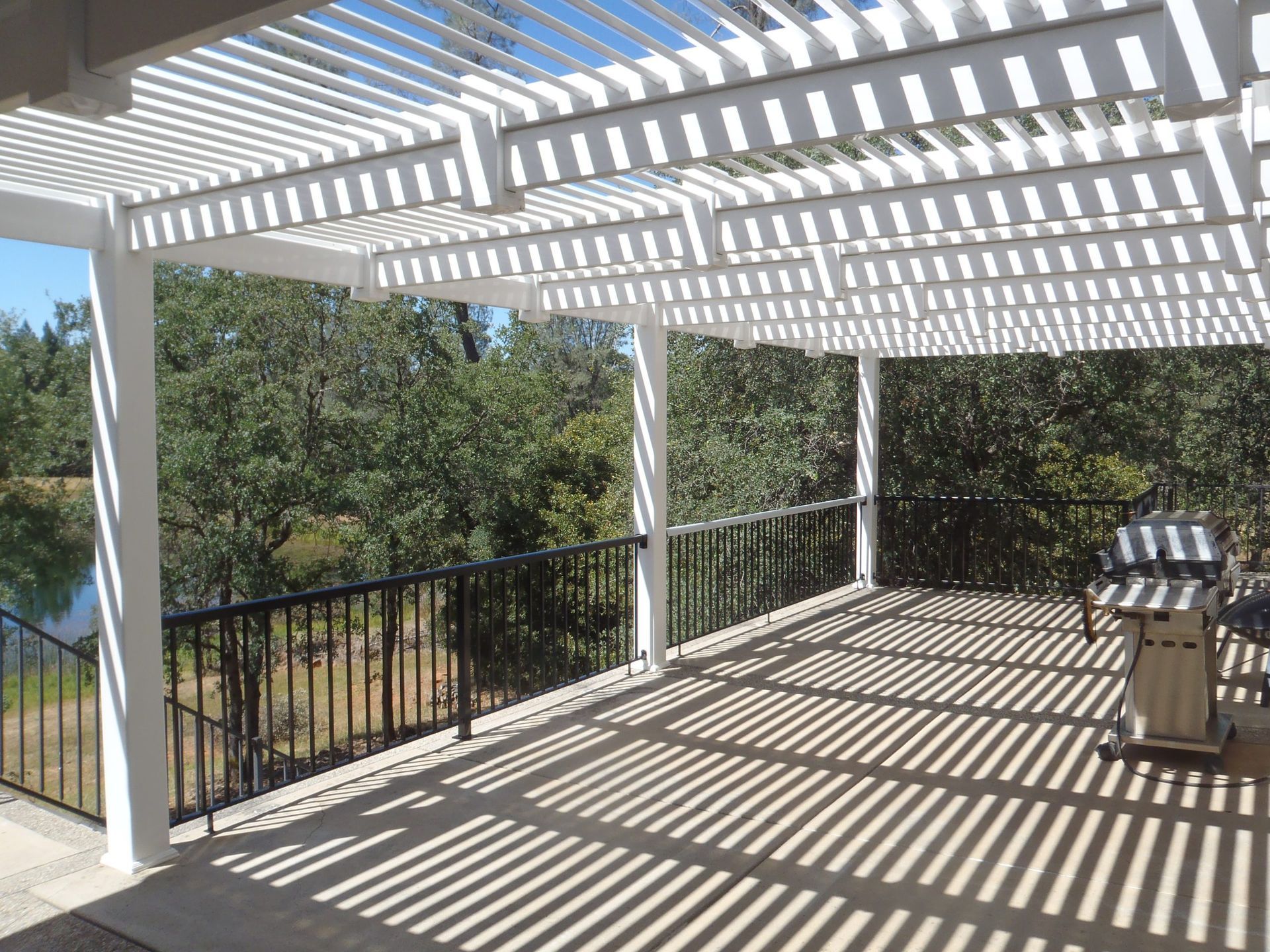 There is a grill on the deck under a pergola.