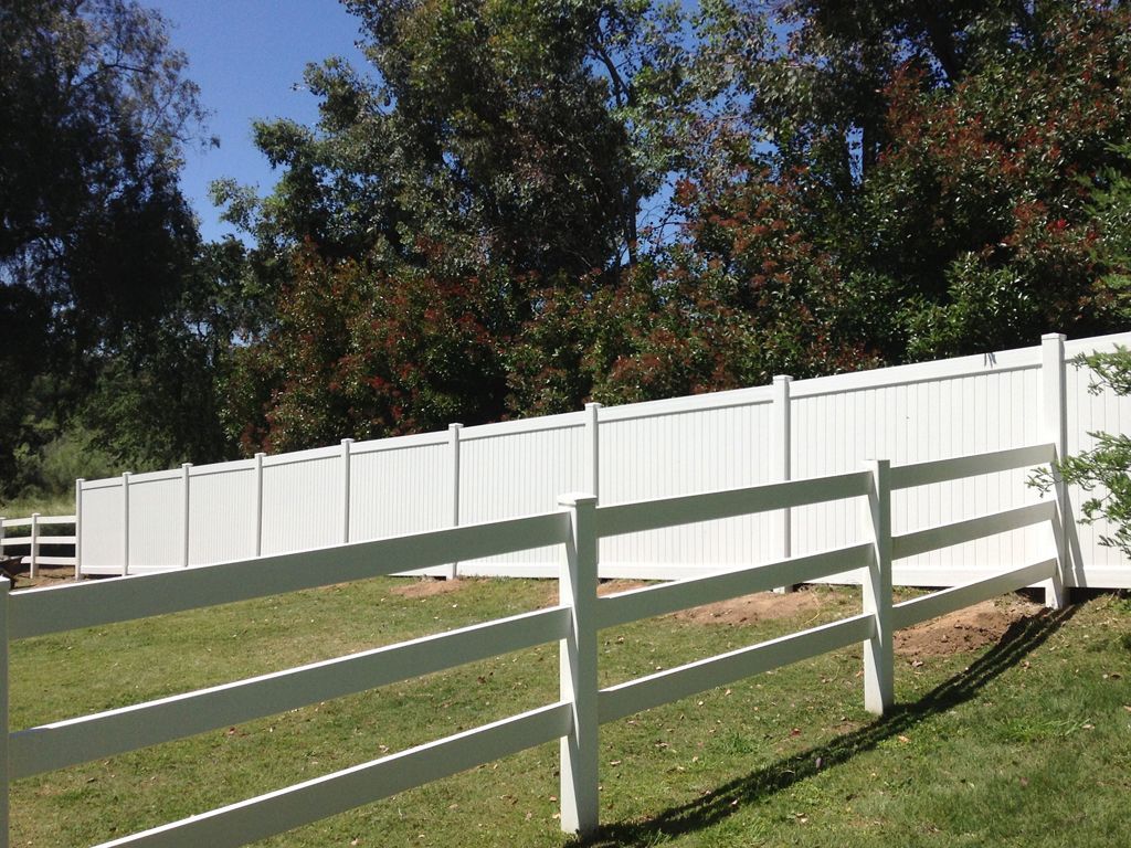 A white fence surrounds a grassy field with trees in the background.