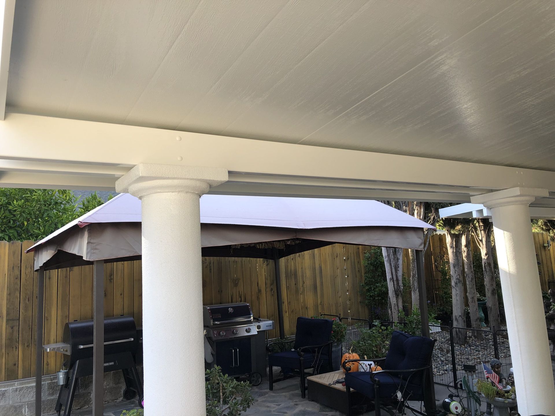 A patio with a gazebo and a grill under a covered patio.