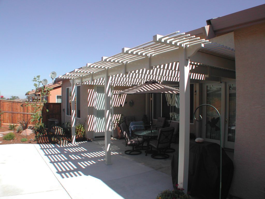 A patio with a pergola and umbrellas in front of a house