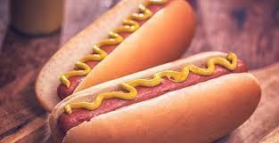 Twee hotdogs in broodjes, besprenkeld met gele mosterd, op een houten ondergrond.