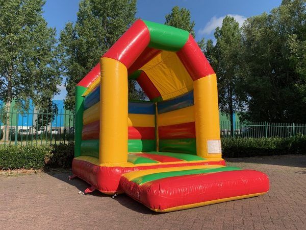 Kleurrijk opblaasbaar springkussen met rode, gele en groene strepen op een verharde ondergrond, buiten.