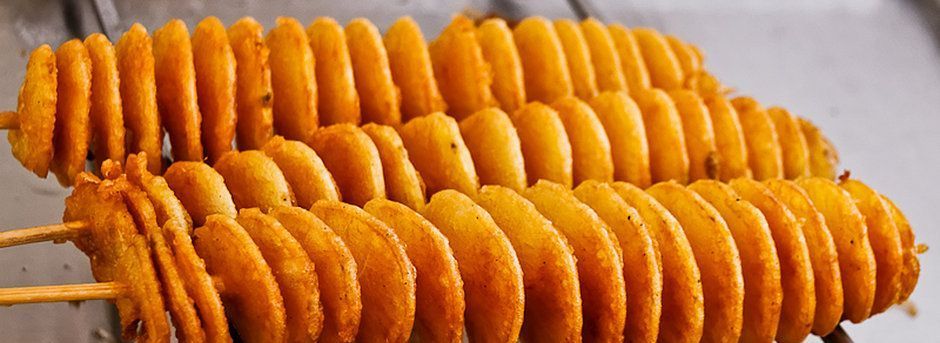 Drie gefrituurde, spiraalvormig gesneden aardappelen aan spiesjes.