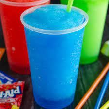 Blauwe, bevroren slushy in een doorzichtige plastic beker, met rode en groene slushies op de achtergrond.