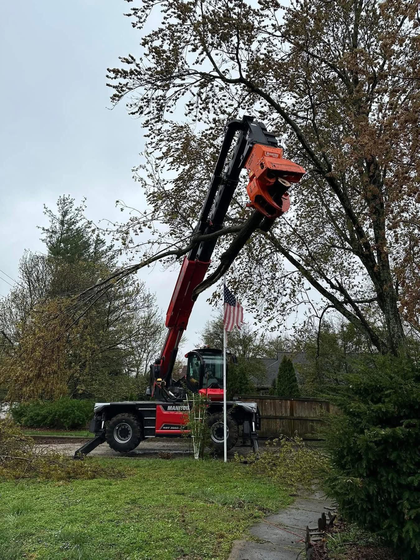 Truck-mounted cherry picker lifting a worker among tall trees in a grassy yard