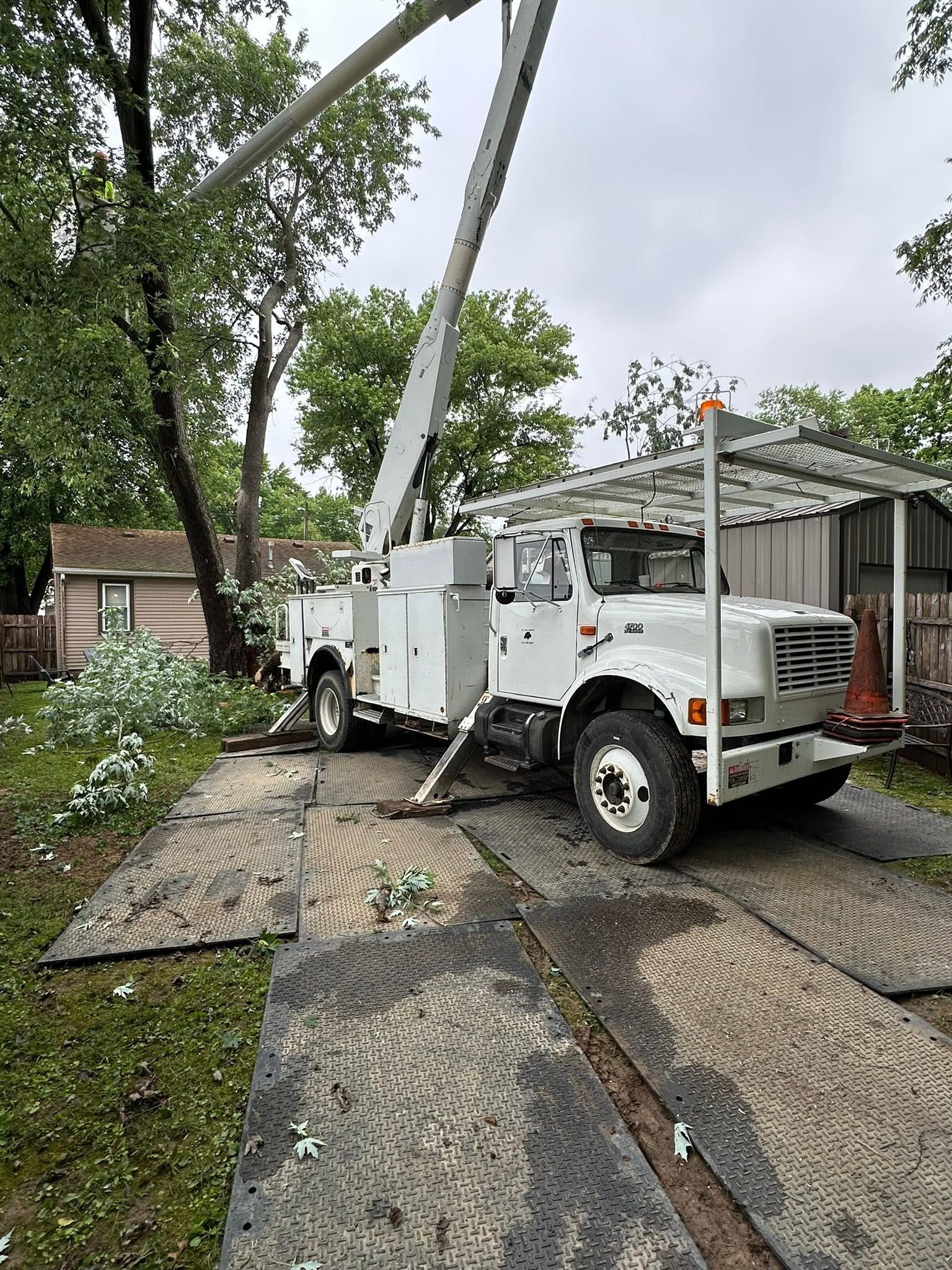 White utility truck with raised boom parked on a muddy driveway beside a house after rain.