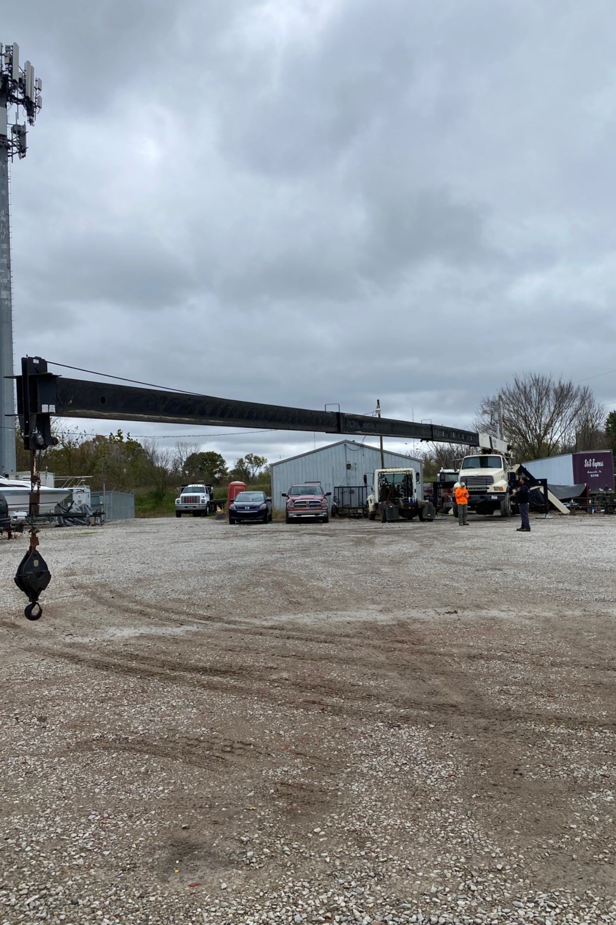 Overcast gravel lot with parked cars and a long black boom arm or crane in the foreground