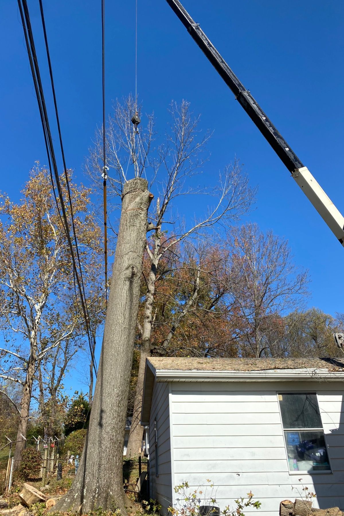 Utility pole being removed beside a white house under a clear blue sky