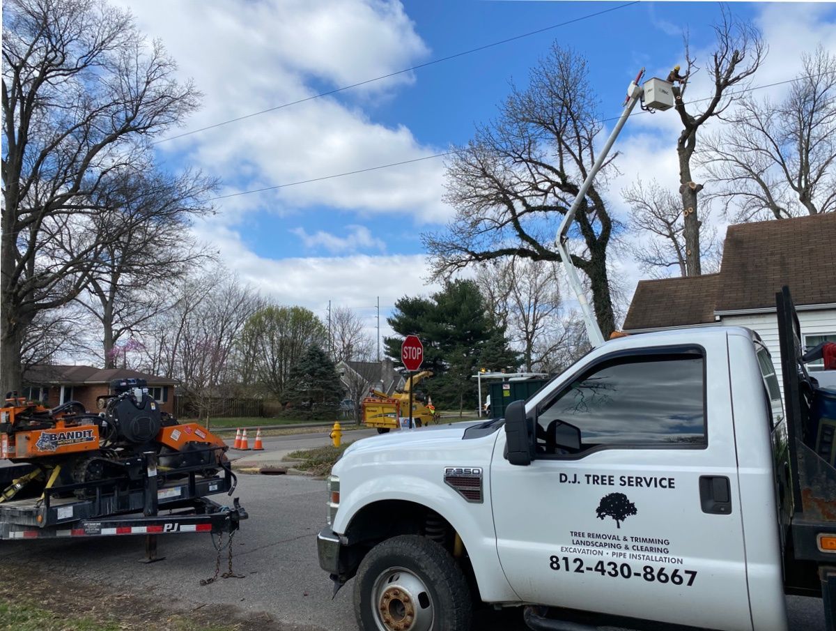 White tree service truck towing orange equipment on a trailer at a road intersection under cloudy sky