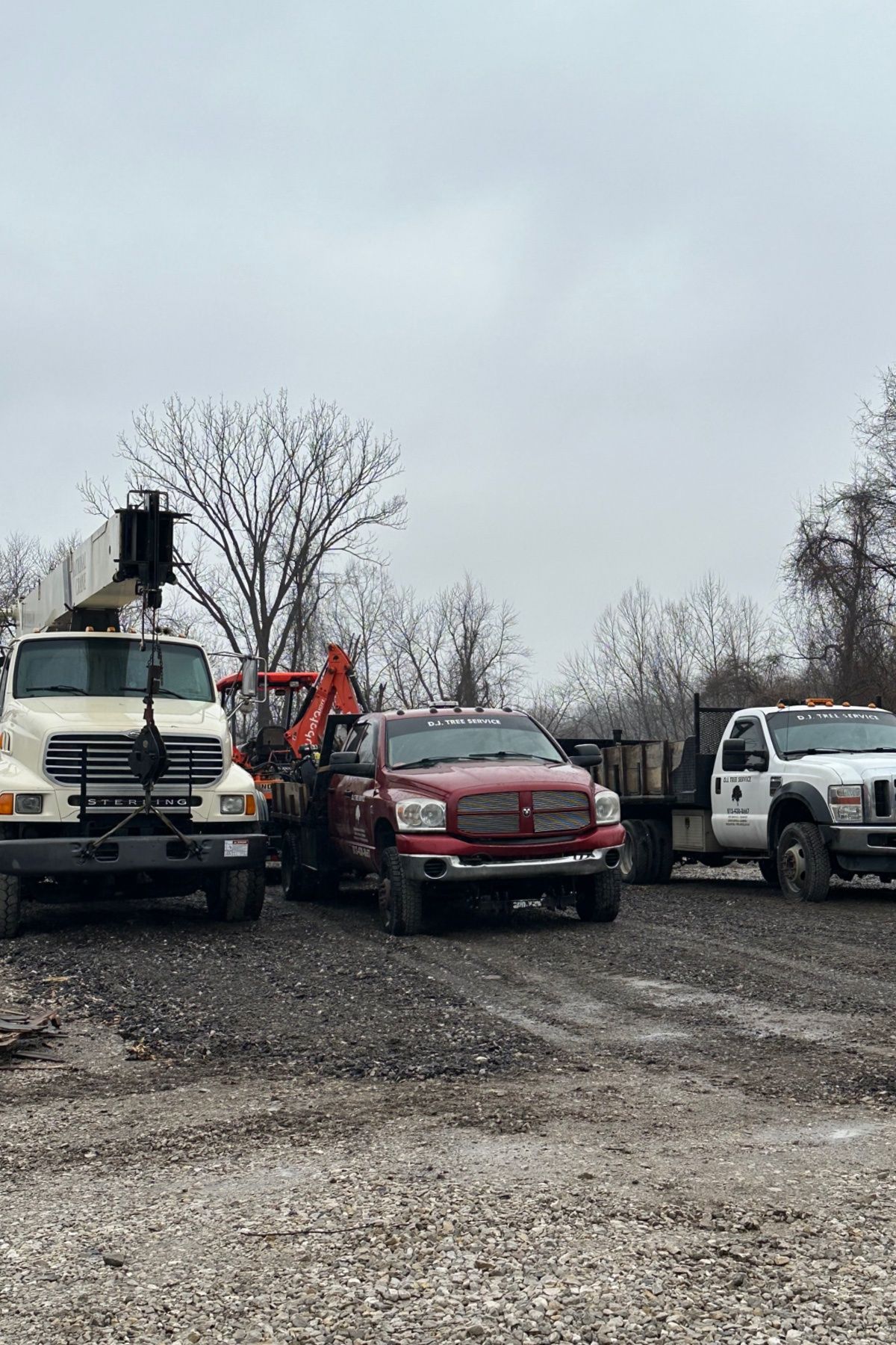 Three work trucks parked on a gravel lot under a cloudy sky