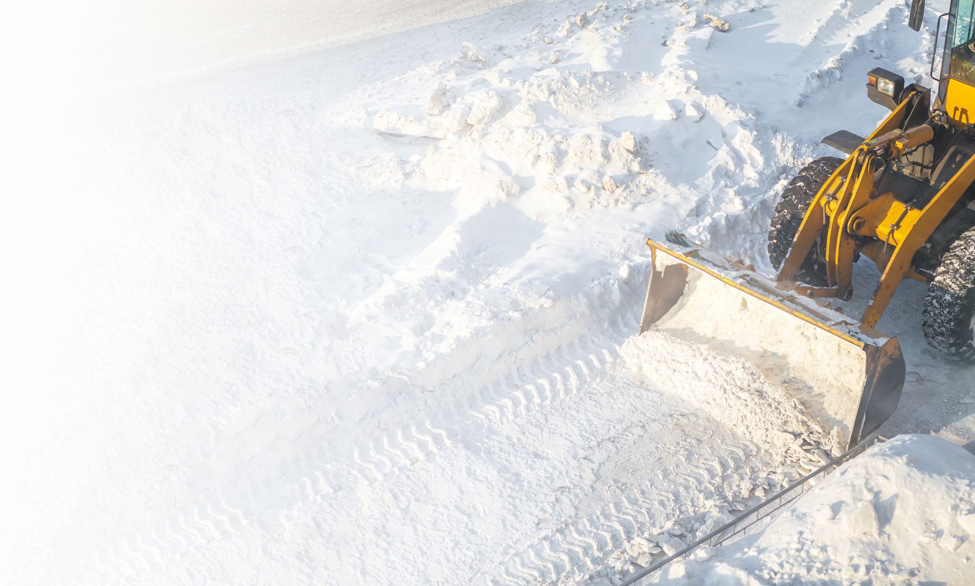 Yellow snowplow clearing a snowy road, spraying snow to the left