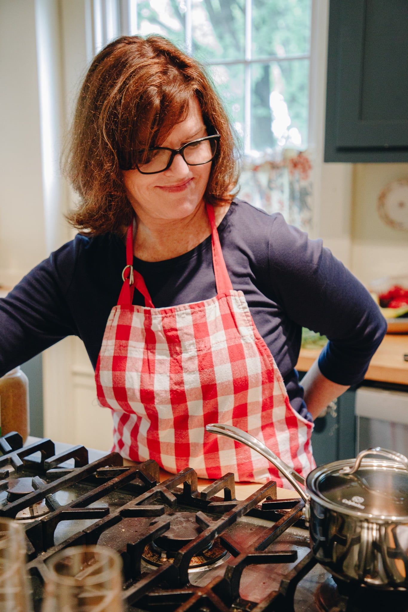 A woman in an apron is standing in front of a stove.