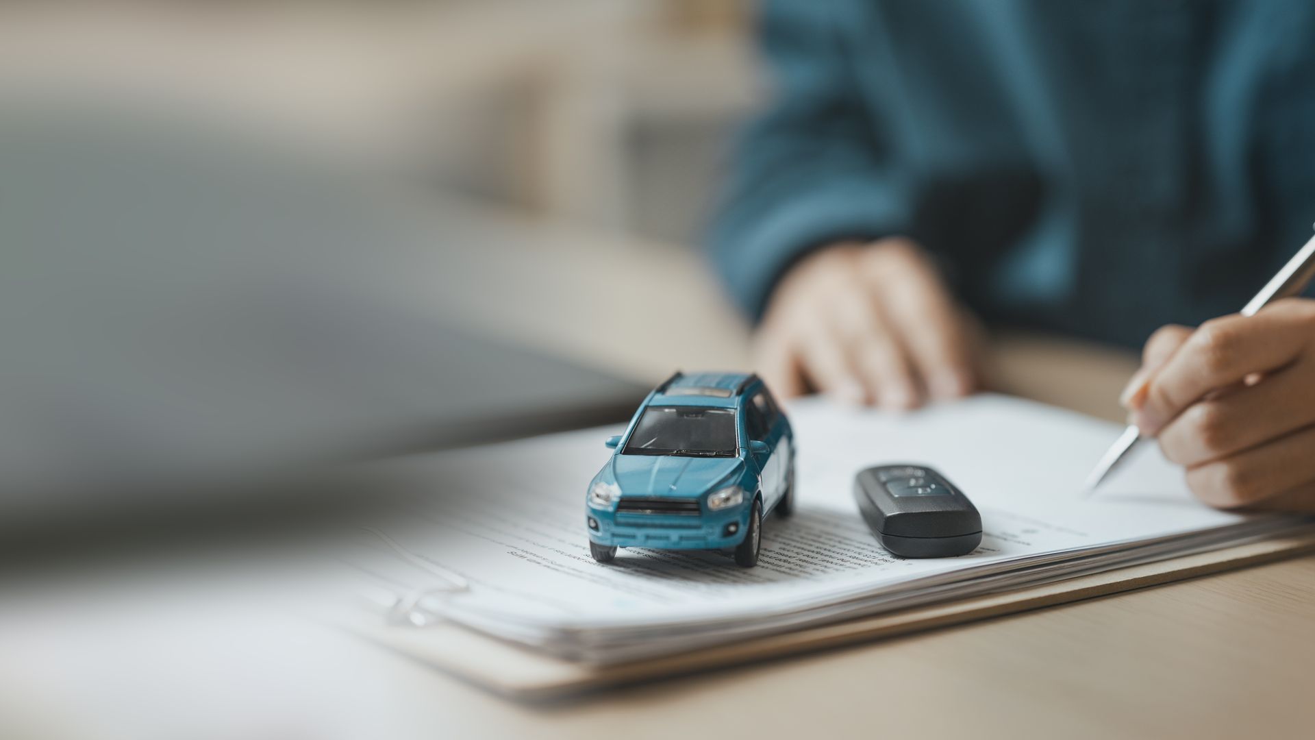 Businessperson signing car purchase agreement with vehicle model.