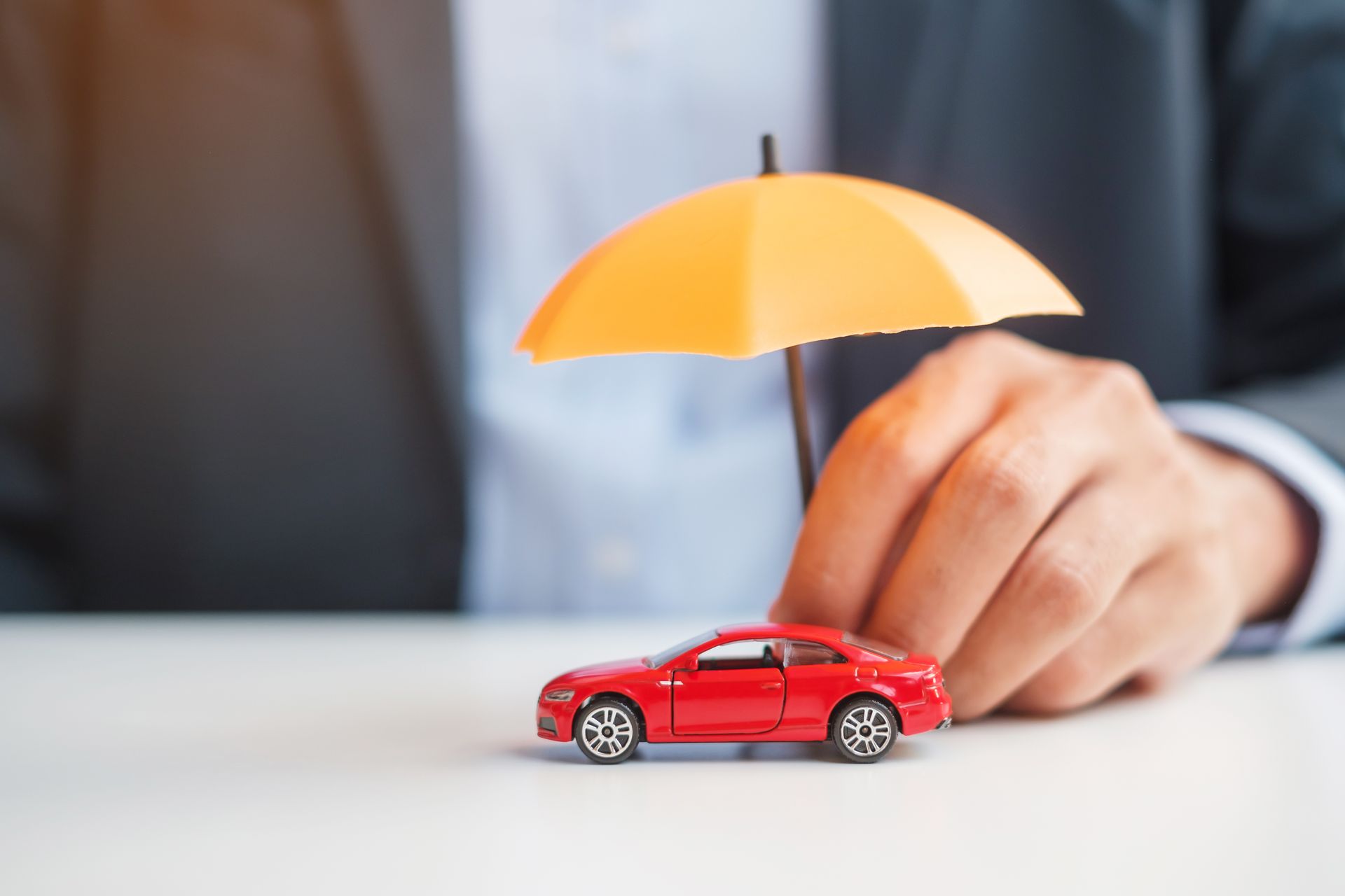 Hand placing a yellow umbrella over a red toy car on a white surface Hand placing a yellow umbrella over a red toy car on a white surface