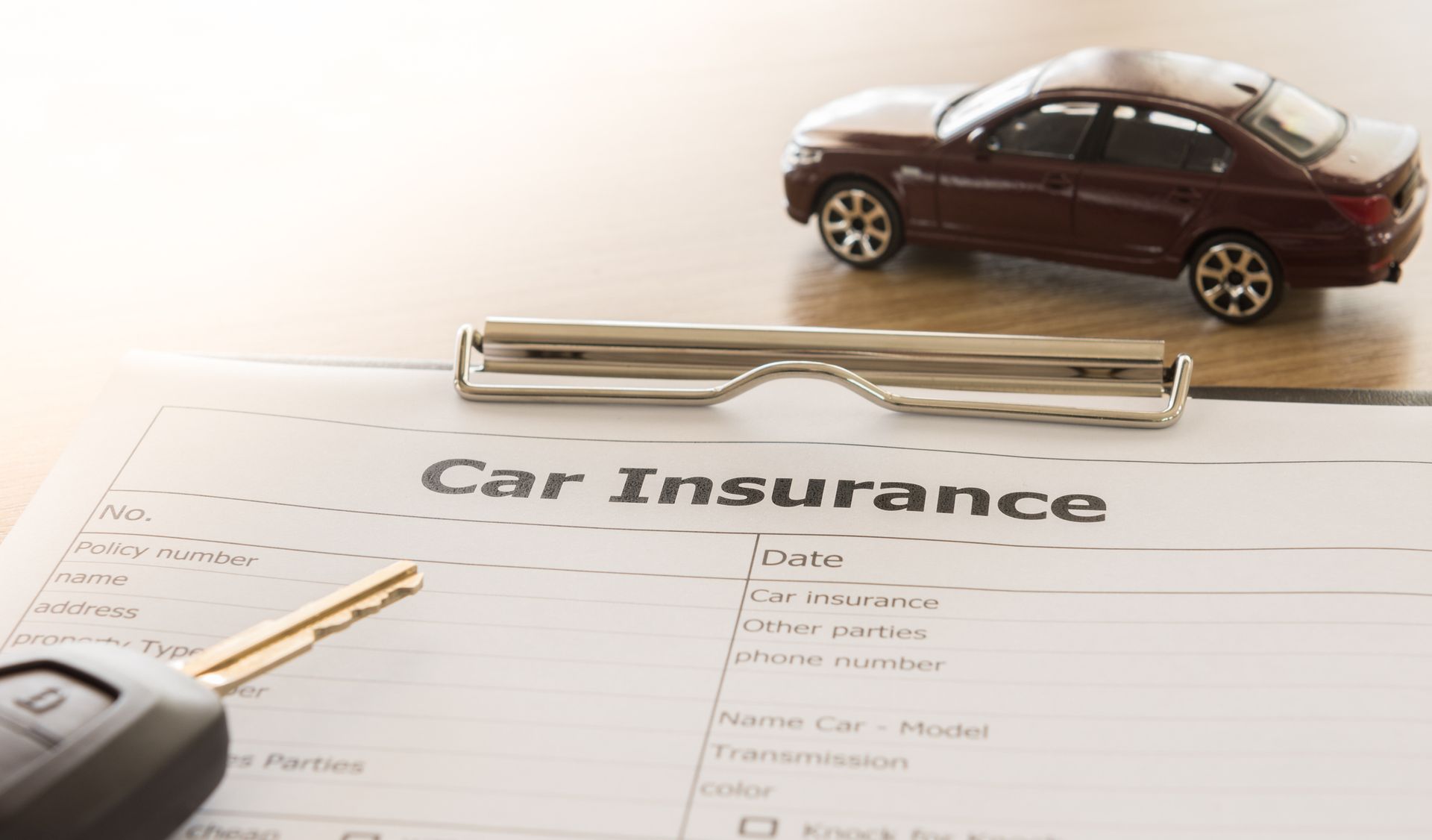 A car insurance application form with a brown car model and a key remote on a desk.