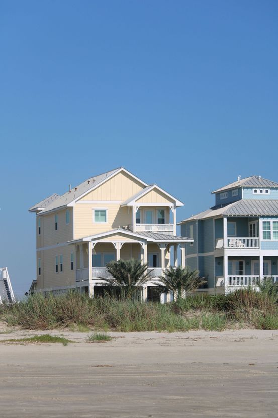 Beachfront houses on stilts near a sandy shore under a clear blue sky