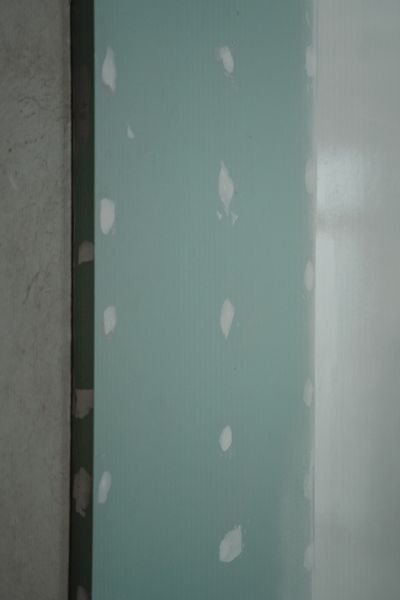 Green drywall panel with white joint compound patches beside a dark wall