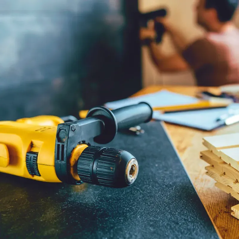 A yellow and black drill is sitting on a wooden table.