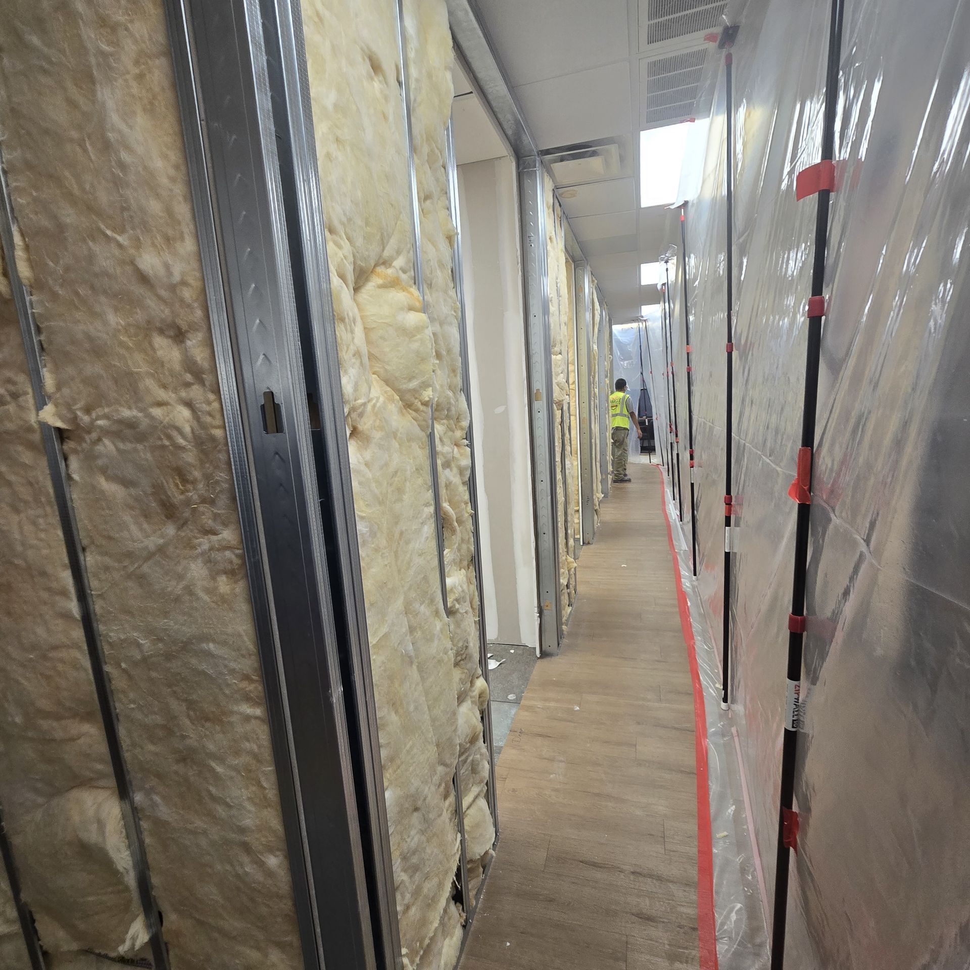 Construction worker in orange hard hat painting a wall with a roller. Interior setting, large windows.
