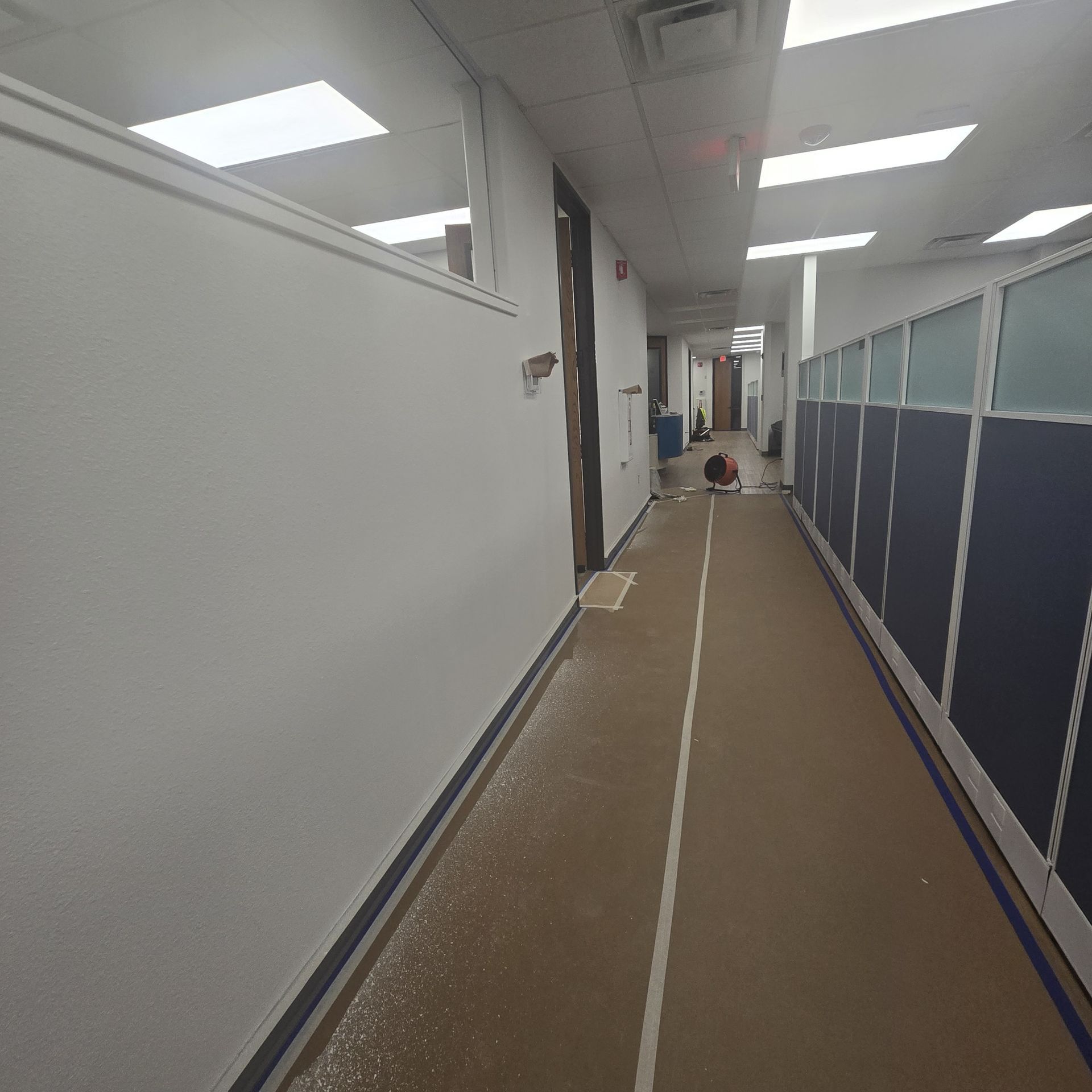 Interior renovation in progress, two workers, exposed ceiling, unfinished walls, large windows.
