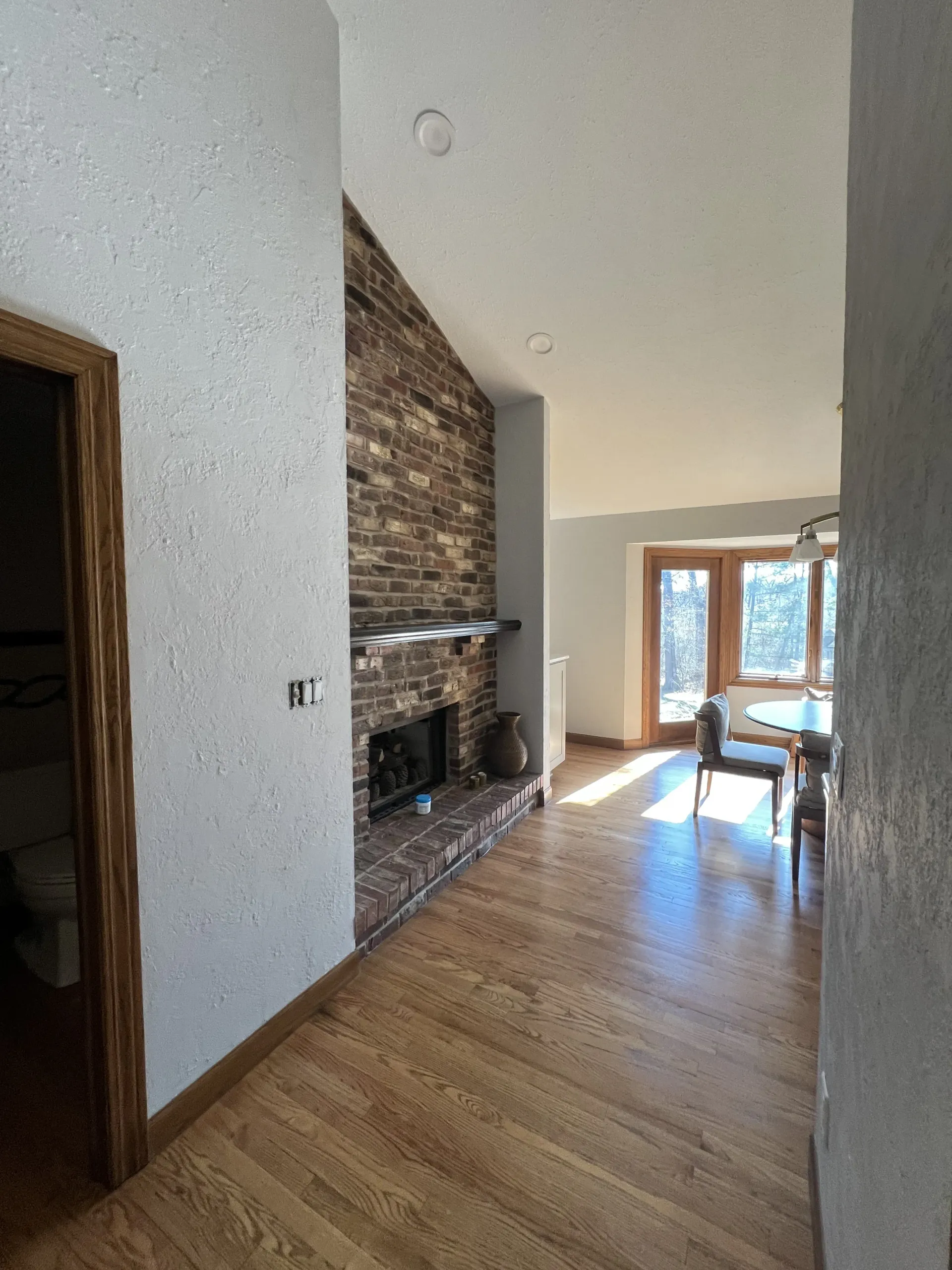 Bright hallway with brick fireplace, hardwood floors, and a table by glass doors leading outside