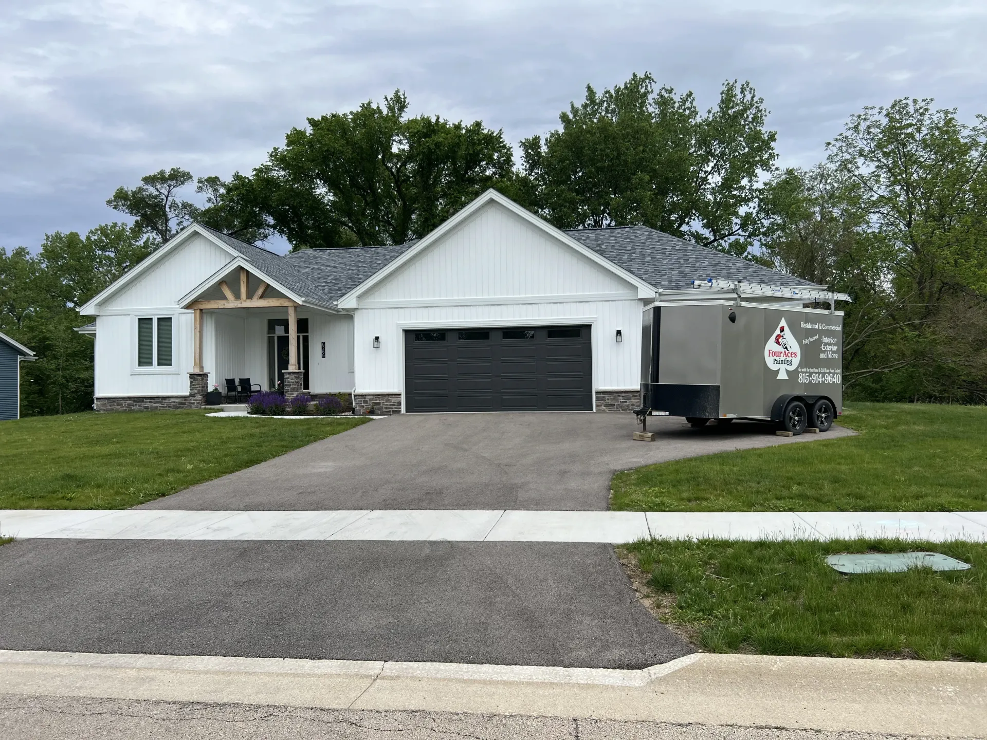 White house with dark garage door and driveway, with a utility trailer parked on the right.