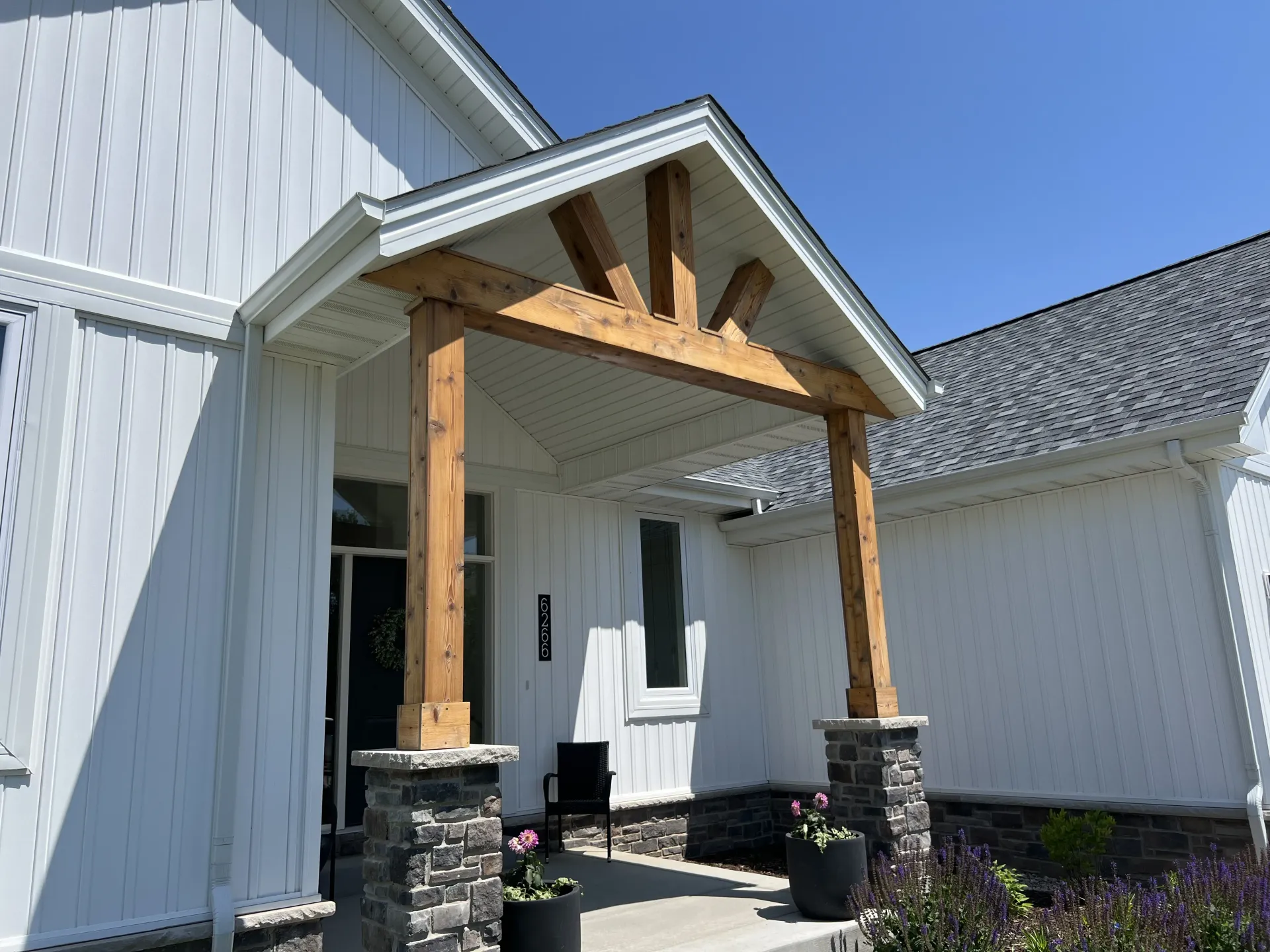 White farmhouse porch with wood posts, a gabled roof, and two planters by the entrance