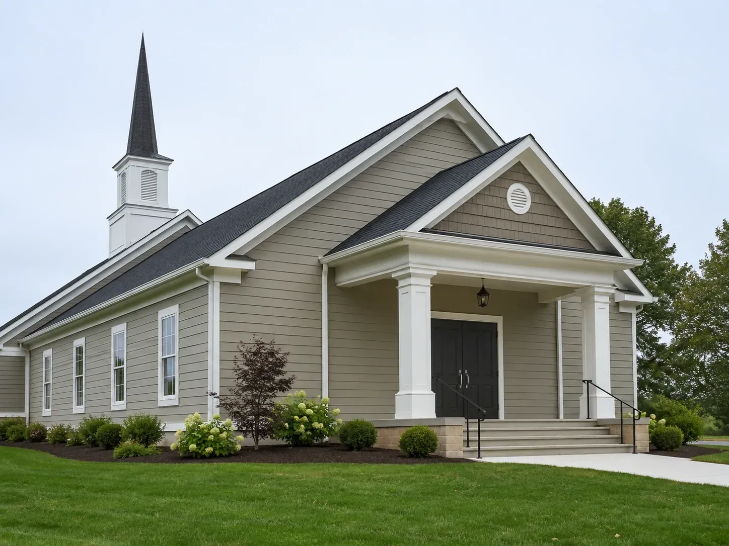 White church with steeple, gray siding, and a covered entrance on a grassy lawn.
